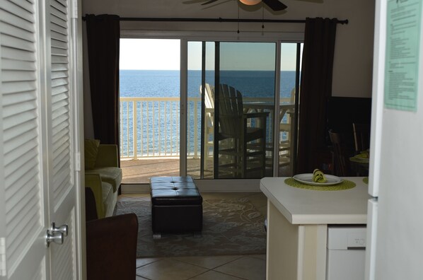 A room with a view of the ocean, a sliding glass door, a dining area with a table and chairs, and a small kitchenette. - BOOK NOW! 4TH FLOOR-BEACH FRONT- TRADEWINDS (Orange Beach)