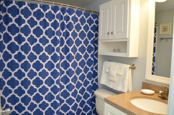 A bathroom with a blue and white patterned shower curtain, a white toilet, a beige sink, and a white cabinet above the sink.