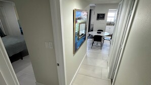 A hallway with a dining area, a bed, and a painting on the wall.