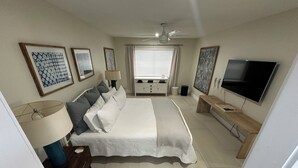A bedroom with a bed, bedside tables, a TV, a ceiling fan, and artwork on the walls.