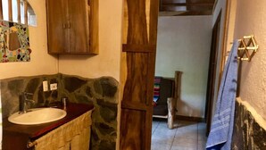 A bathroom with a stone wall, wooden cabinets, a sink, and a towel rack. - Rancho el Rio: Nature, Riverside & Farm (Monteverde)