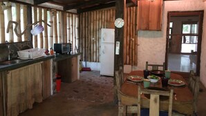 A rustic kitchen with wooden walls, a dining table with chairs, a refrigerator, and a microwave. - Rancho el Rio: Nature, Riverside & Farm (Monteverde)