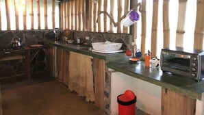 A rustic kitchen with a stone wall, wooden beams, and a built-in stove. - Rancho el Rio: Nature, Riverside & Farm (Monteverde)