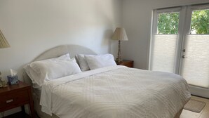 A neatly made bed with white linens in a room with a wooden nightstand, a lamp, and a window with blinds. - Private Cottage, Amazing Gardens within a Gated Estate  - True European Charm! (Soquel)