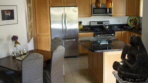 A modern kitchen with wooden cabinets, stainless steel appliances, and a dining area with a table and chairs. - Private Cottage, Amazing Gardens within a Gated Estate  - True European Charm! (Soquel)