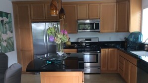 A modern kitchen with wooden cabinets, stainless steel appliances, and a central island with a vase of flowers. - Private Cottage, Amazing Gardens within a Gated Estate  - True European Charm! (Soquel)