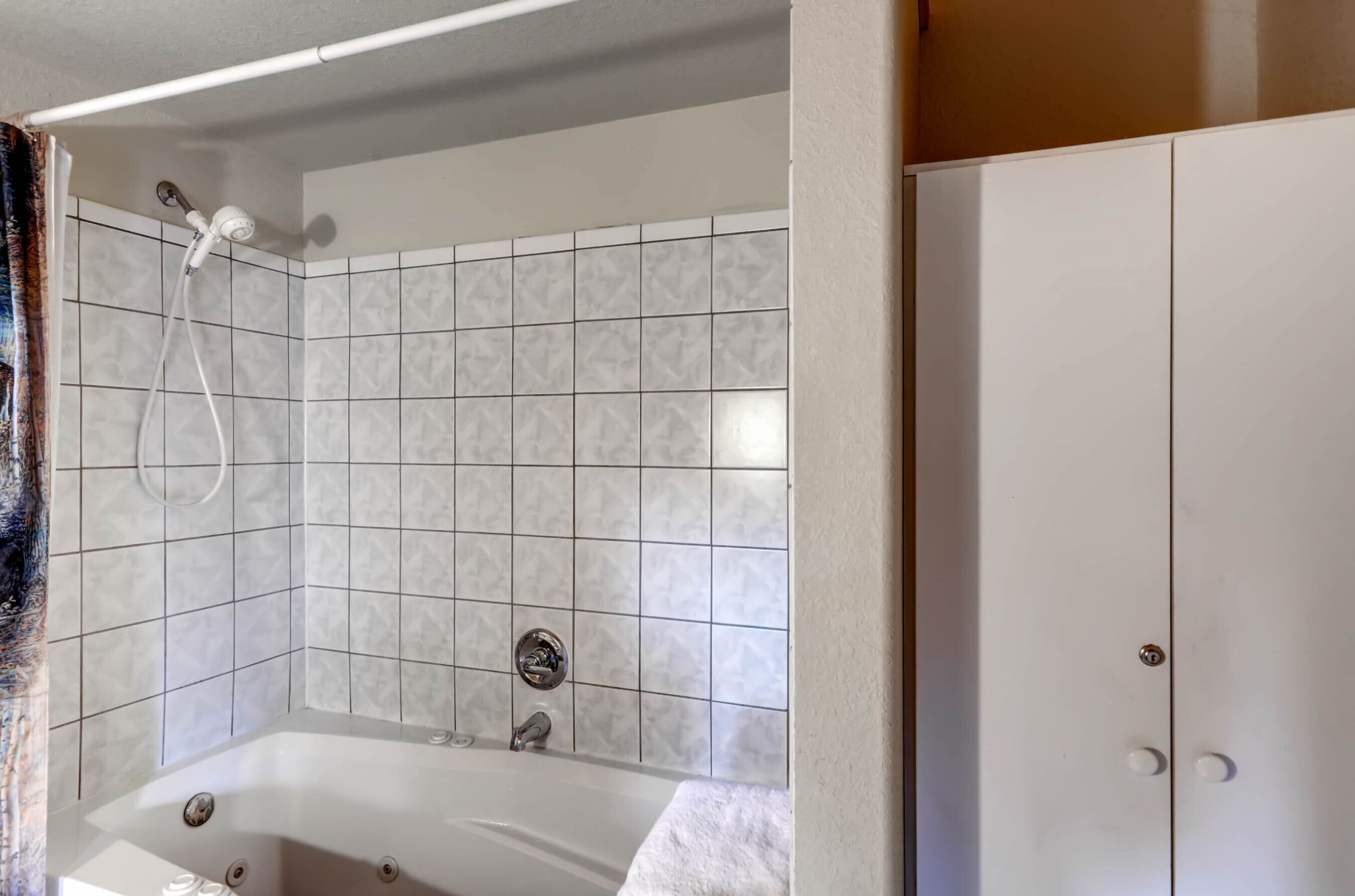A bathroom with a bathtub, a shower, and a white tiled wall.