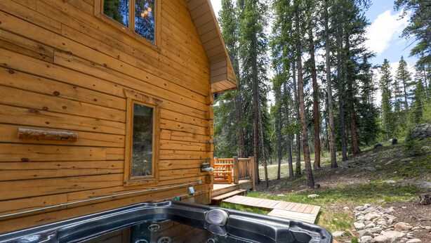 Une cabane en bois dotée d’un bain à remous et d’une terrasse offrant une vue sur une zone boisée.