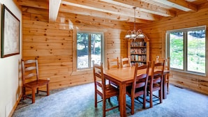 L’intérieur d’un chalet en bois comprend une table à manger, des chaises, une bibliothèque et de grandes fenêtres.