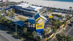 A coastal hotel with a prominent yellow and blue sign, a parking lot, and a beach view. - AMAZING BEACH VIEWS! Next to Gulf State Park (Gulf Shores)