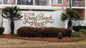 The Grand Beach Resort sign with a white background and gold lettering. - AMAZING BEACH VIEWS! Next to Gulf State Park (Gulf Shores)