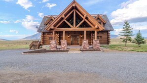 Une cabane en rondins avec un toit triangulaire, une véranda à l’avant et une allée gravillonnée.