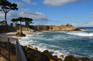 A coastal scene with rocky cliffs, a sandy beach, and waves crashing onto the shore. - Oceanfront Home with Spectacular Views on Monterey Bay.  (Pacific Grove)