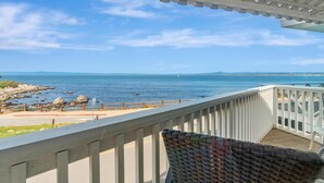 Ein Balkon mit Blick auf das Meer, einem weißen Geländer und einem Korbstuhl.