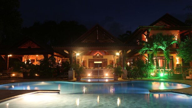 A nighttime view of a resort with a swimming pool, a gazebo, and a building with a traditional architectural style. - Sunrise Villa - An affordable beachfront gathering place for family and friends (Cabrera)