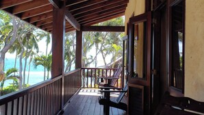 A wooden deck with a railing overlooking a pool and palm trees, leading to a door. - Sunrise Villa - An affordable beachfront gathering place for family and friends (Cabrera)