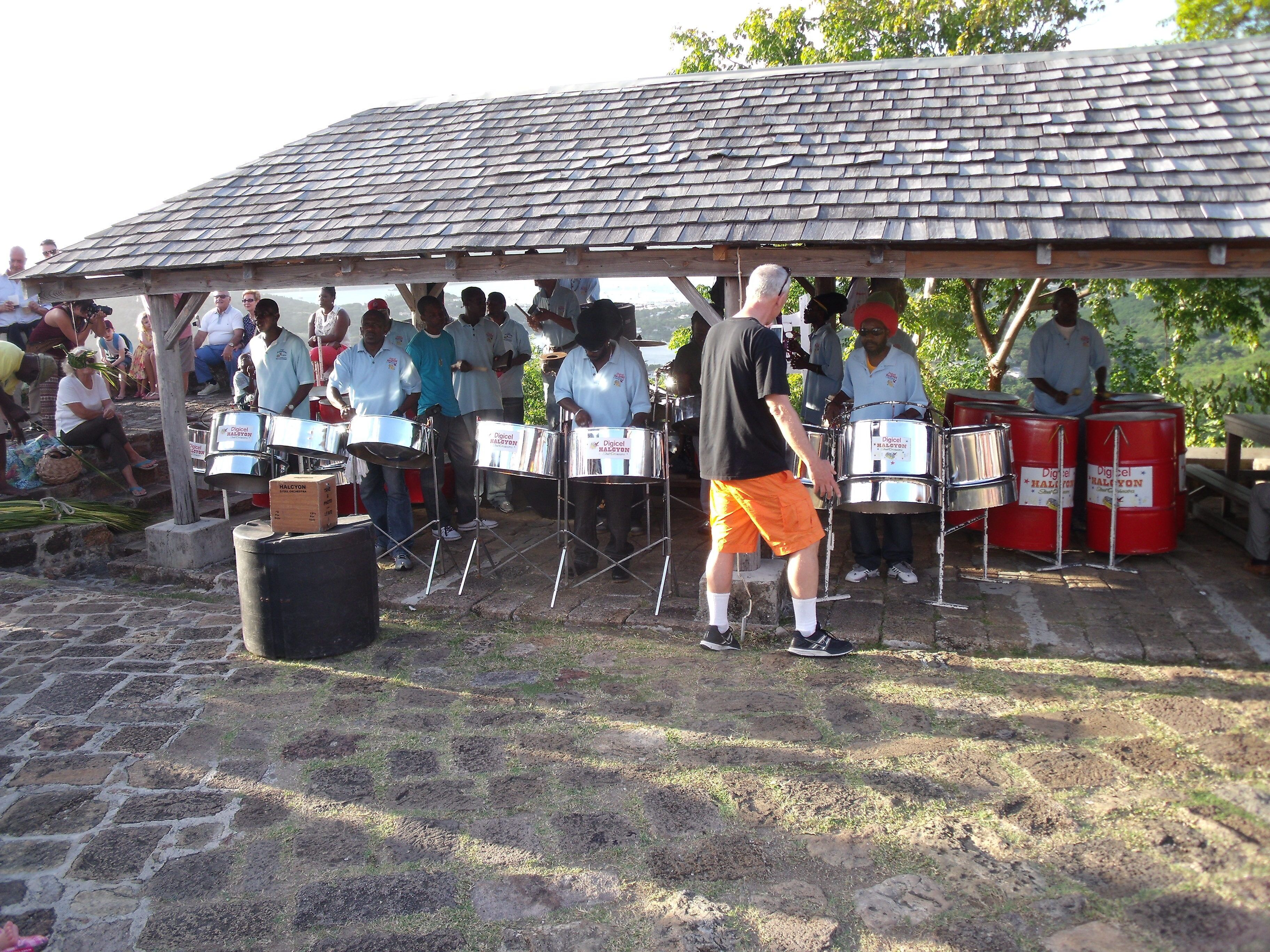 A group of people under a covered area with a tiled roof, some seated and some standing, possibly at an event or gathering.