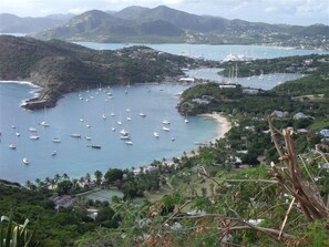 A coastal area with numerous sailboats anchored in a bay surrounded by lush greenery and hills.