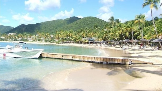 Una playa con muelle de madera, agua cristalina y palmeras.