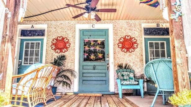 A porch with a wooden floor, a blue door, and a ceiling fan. There are two chairs and a bench on the porch. - 2brCoastalColonialApt between Jekyll & St Simons Islands beaches& near Downtown! (Brunswick)