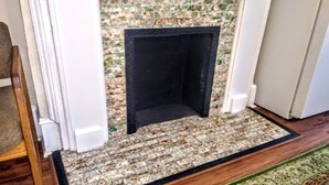 A fireplace with a mosaic surround, a wooden floor, and a green area rug. - 2brCoastalColonialApt between Jekyll & St Simons Islands beaches& near Downtown! (Brunswick)
