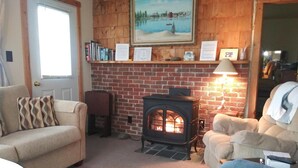 Una sala de estar acogedora con chimenea de ladrillo, un sofá, una butaca y una estantería.