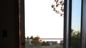 Una habitación con una cama, una puerta que da al exterior y vistas a un campo cubierto de hierba con árboles y una masa de agua al fondo.