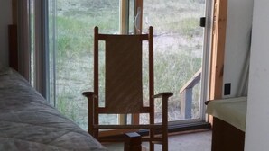 Una habitación con una cama, una mecedora de madera y un amplio ventanal corredera que da a un jardín.