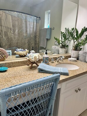 Un baño con encimera de granito, lavamanos, espejo, cortina de ducha y plantas en macetas.
