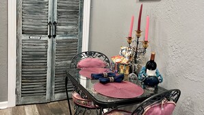 A dining area with a table set for four, featuring a glass top and metal chairs with cushioned seats. A decorative candelabra with candles is on the table.