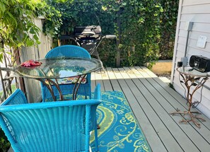 Un patio con mobiliario de mimbre azul, una mesa de vidrio y una parrilla.