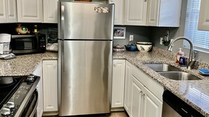 A kitchen with white cabinets, a stainless steel refrigerator, a microwave, a stove, and a sink.