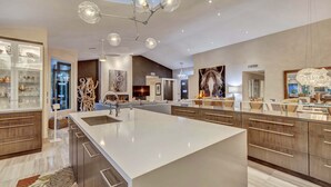 Een moderne keuken met een groot kookeiland, inbouwapparatuur en een eethoek met een tafel met glazen blad.