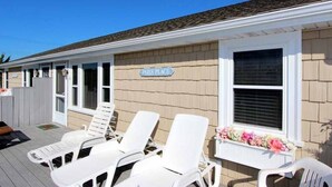 A beach house with a sign reading "PALS PLACE," white lounge chairs, and a window with a flower box.