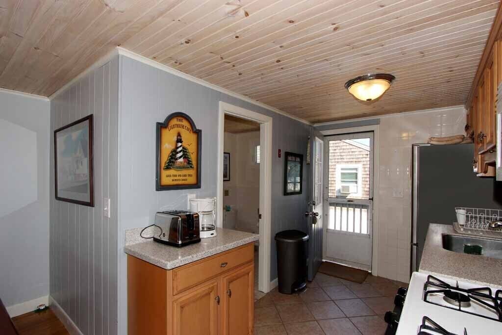 A kitchen with wooden cabinets, a gas stove, a coffee maker, and a trash can.