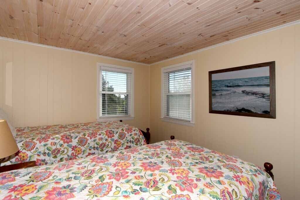 A bedroom with two beds, wooden ceiling, and a beach view.