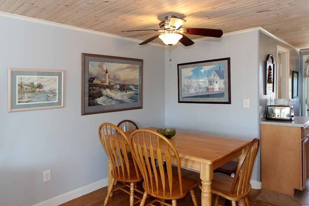 Un coin repas avec une table et des chaises en bois, des œuvres d’art encadrées au mur et un ventilateur de plafond.