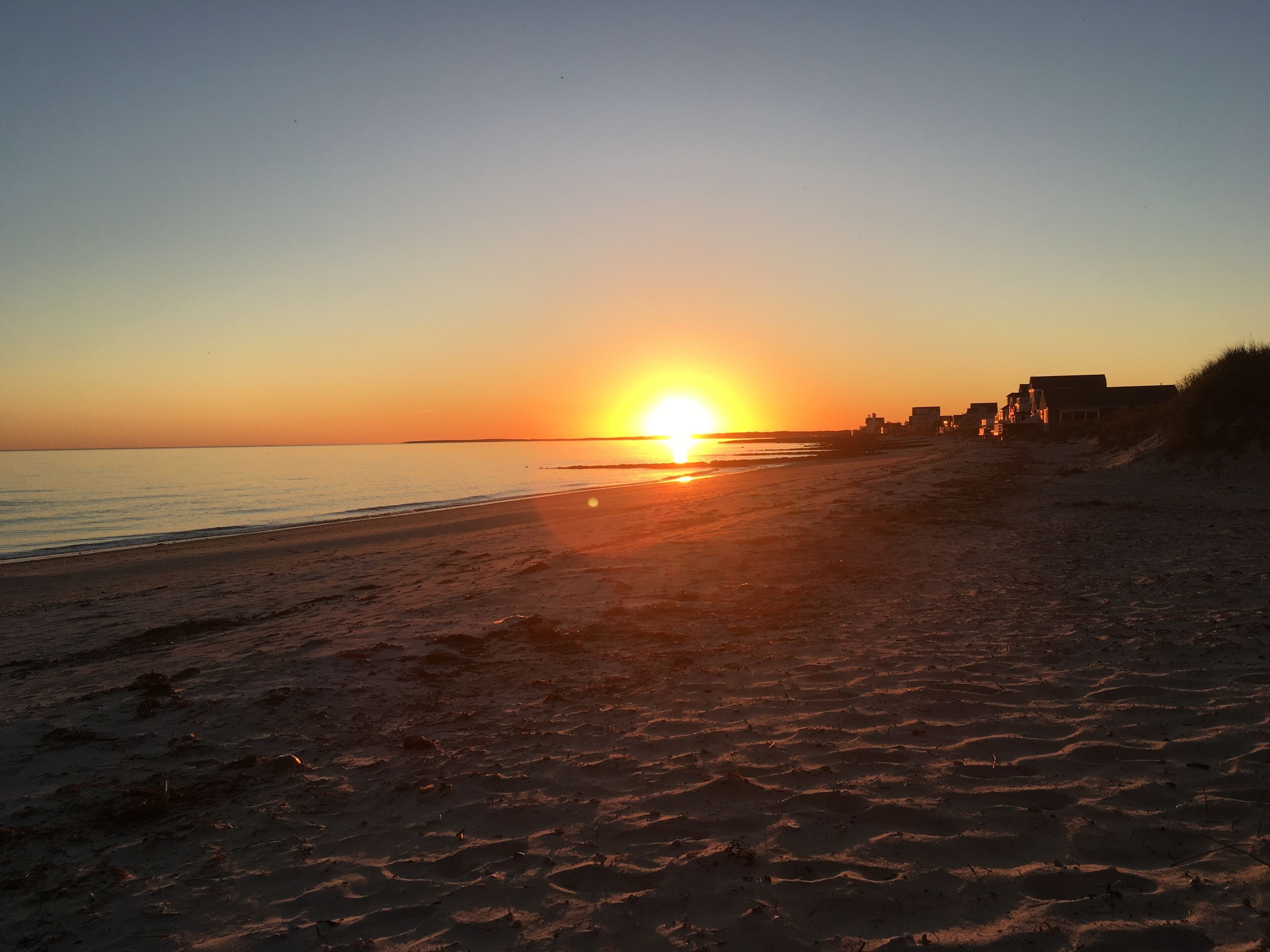 Una playa al atardecer, con el sol bajo en el horizonte, proyectando un brillo cálido sobre la arena y el agua.