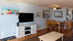 A living room with a flat-screen TV, wooden dining table, and chairs.