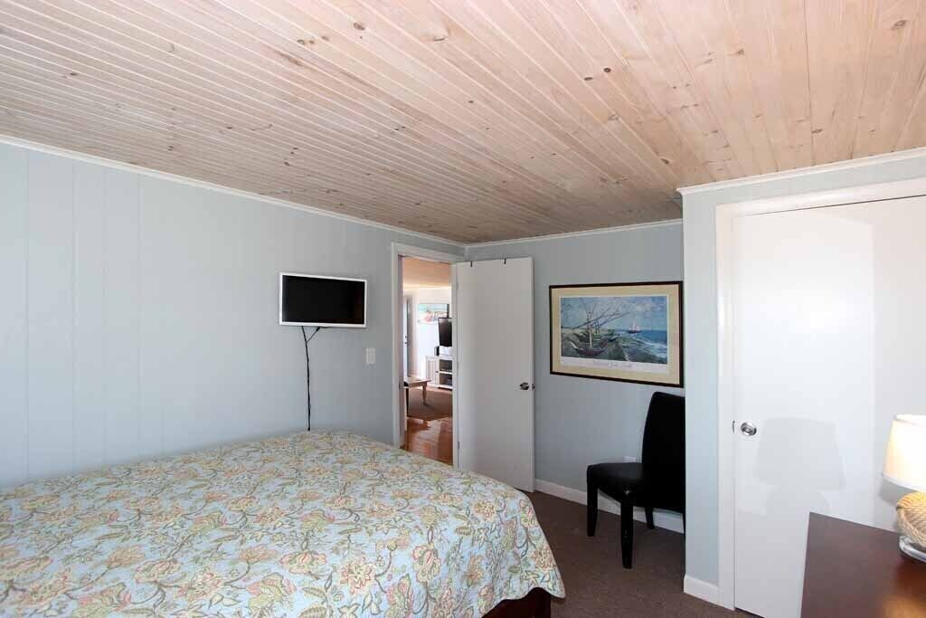 A bedroom with a bed, a TV, a chair, and a door leading to another room.