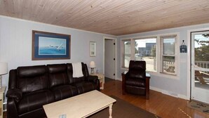 A living room with a dark leather sofa, a wooden coffee table, and a large window with blinds.