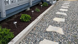 A residential property with a grey deck, a wooden fence, and a gravel pathway with stepping stones.