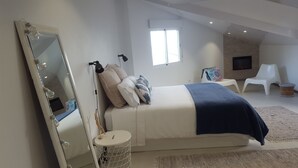 A bedroom with a large mirror, a bed with a blue blanket, a round side table, and a TV in the corner. - Fantastic - Cabo Girão view  (Câmara de Lobos)