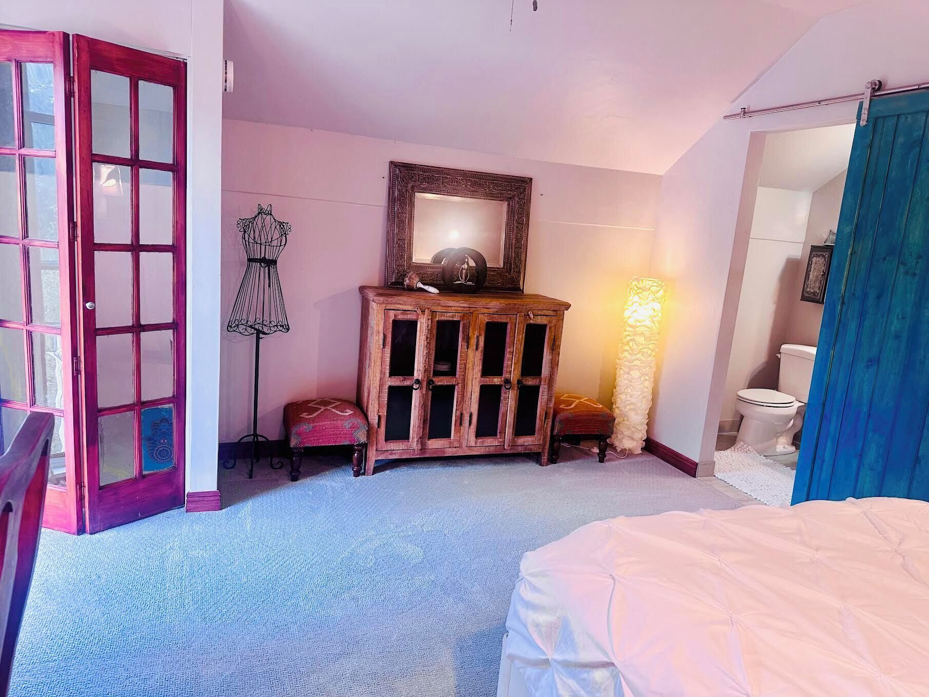 Een slaapkamer met een bed, een houten kast, een spiegel, een vloerlamp en een toilet.