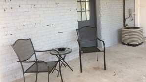 Ein Zimmer mit weißen Ziegelwänden, einem Fenster, einer Tür, einer wandmontierten Leuchte und einem runden, strukturierten Objekt auf dem Boden.