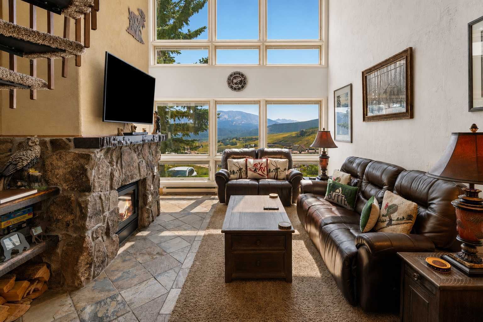 A spacious living room with a fireplace, leather sofas, a coffee table, and large windows offering a mountain view.