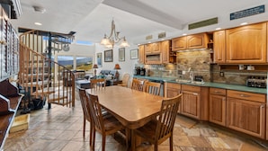 A spacious kitchen with wooden cabinets, a dining table, and a view of the mountains through large windows. - Columbine 2107 (Crested Butte)