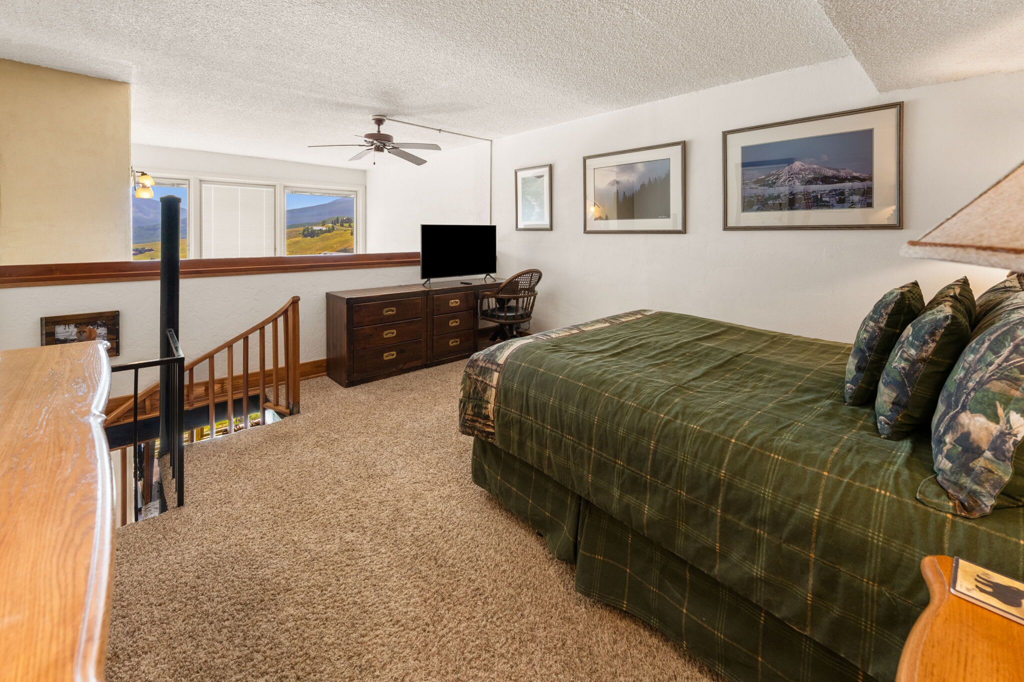 A bedroom with a bed, dresser, television, and a ceiling fan.