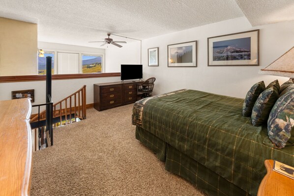 Une chambre à coucher comprenant un lit, une commode, un téléviseur et un ventilateur de plafond.