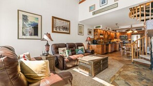 A spacious living room with leather sofas, a coffee table, and a kitchen area with wooden cabinets and a stone backsplash. - Columbine 2107 (Crested Butte)